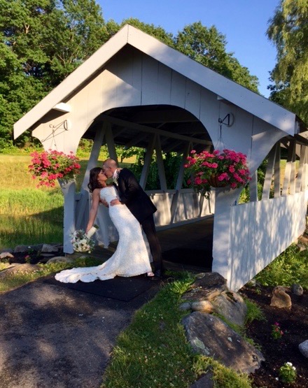 A bride and groom embrace next to a covered bridge on their wedding day at Butternut Farm Golf Club in Stow, Massachusetts